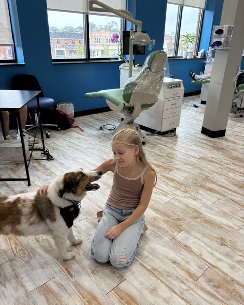 A patient greets the therapy dog beside the dental chair